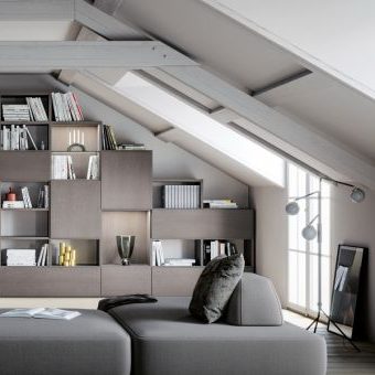 Ein graues Regal an eine Dachschräge angepasst mit offenen und geschlossenen Fächern, im Vordergrund ist ein passendes Sofa